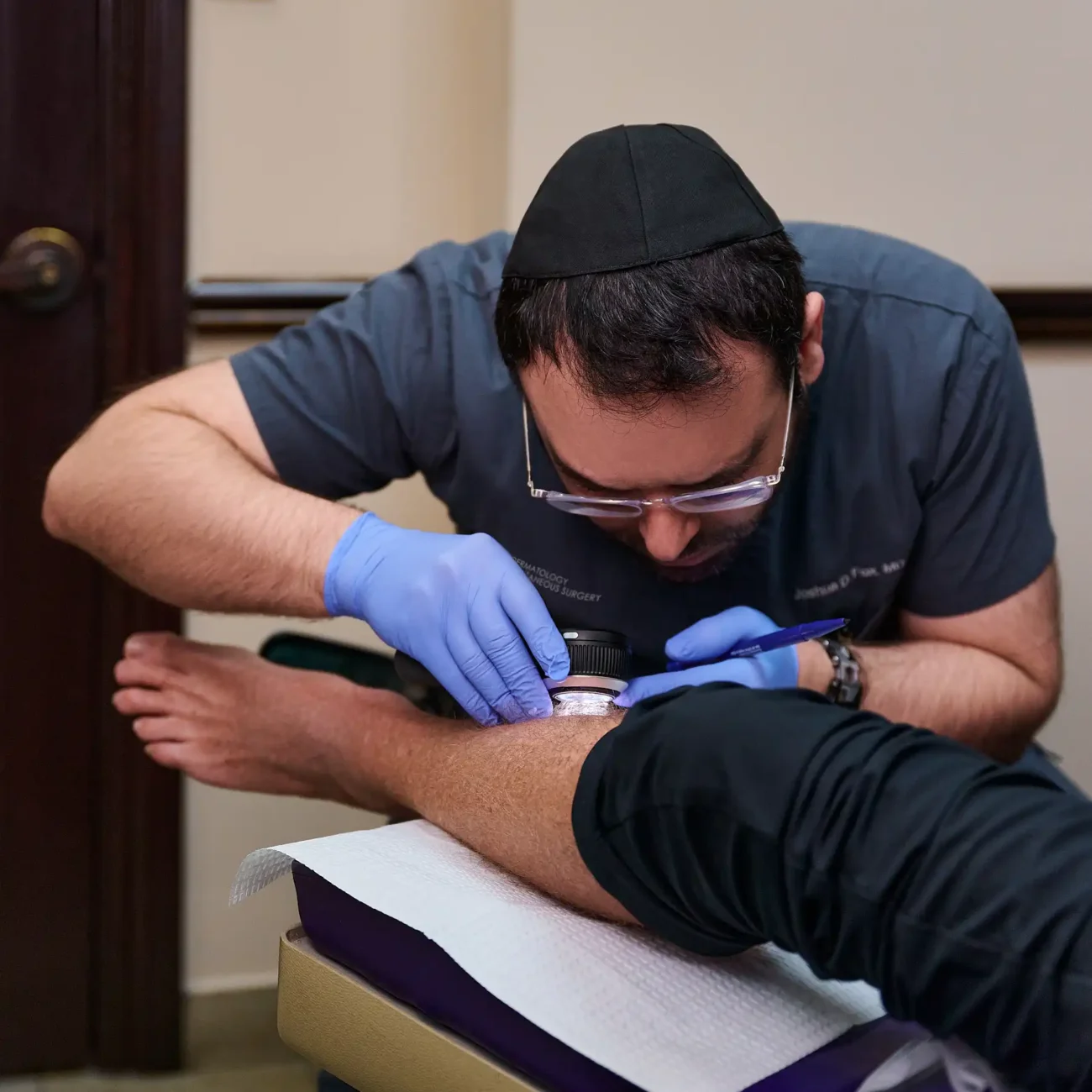 Dermatologist treating a patient's foot in a clinical setting, wearing protective gloves.