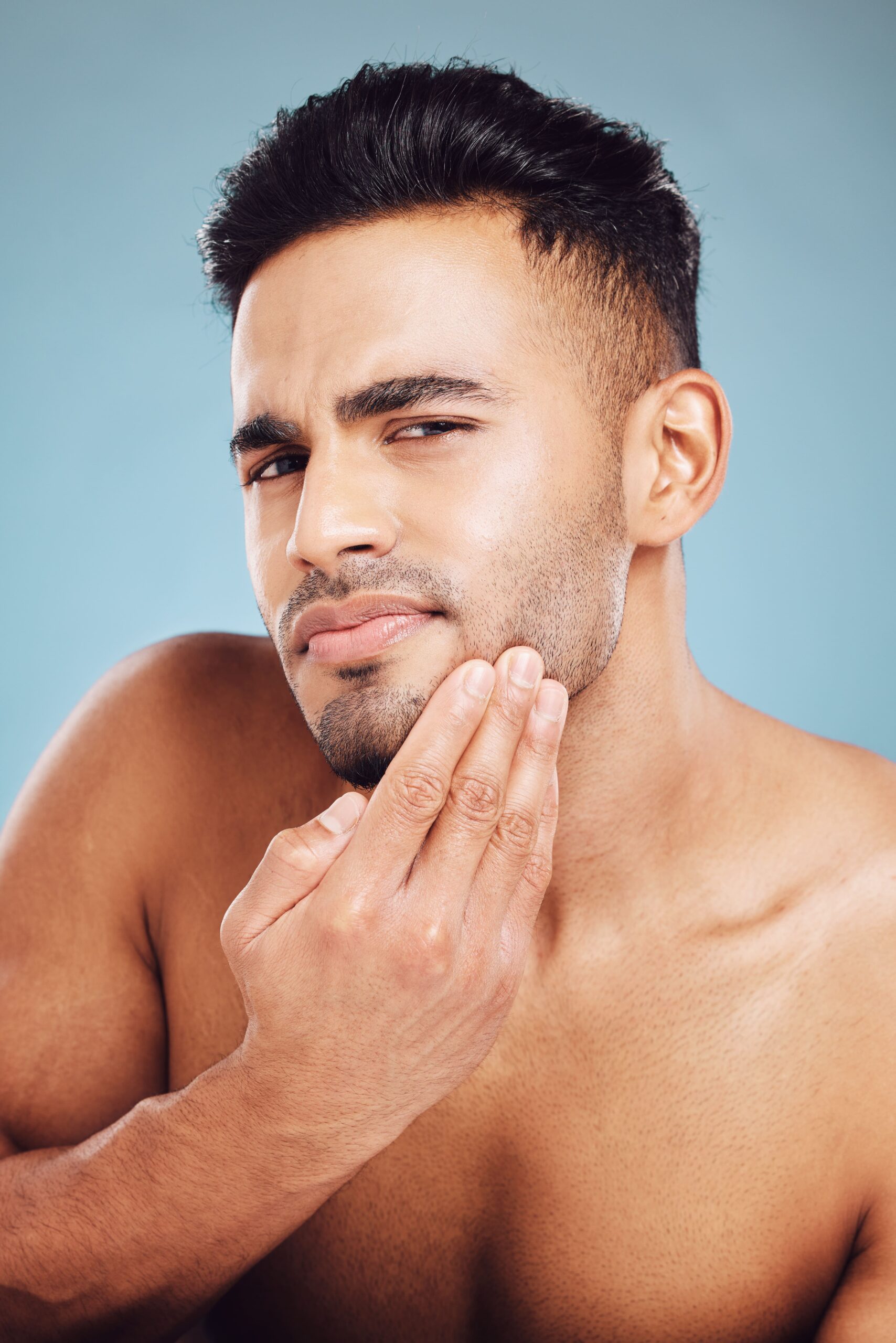 Man with thoughtful expression touching his face against a soft blue background.